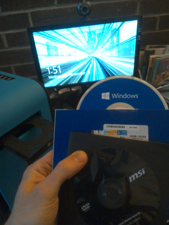 Holding the Windows 8.1 and MSI DVDs in front of the monitor showing a Windows lock screen.